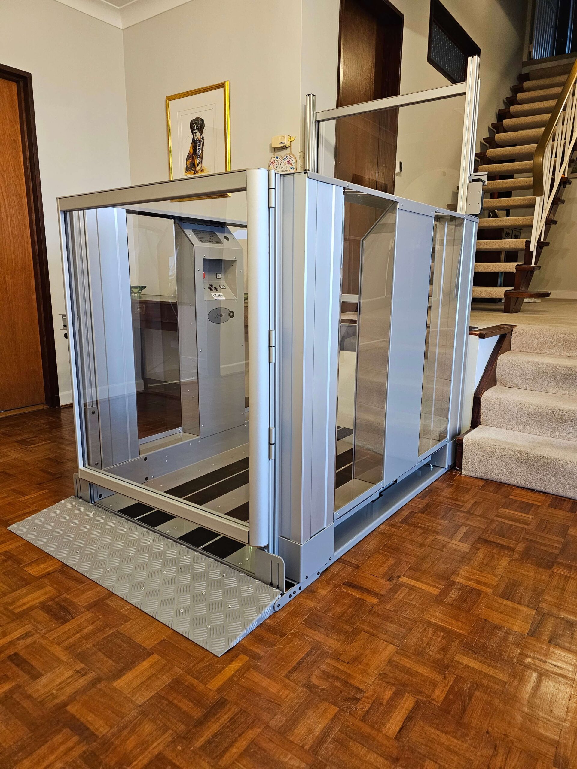 Platform lift in silver aluminium with a ramped entrance in a split-level hallway