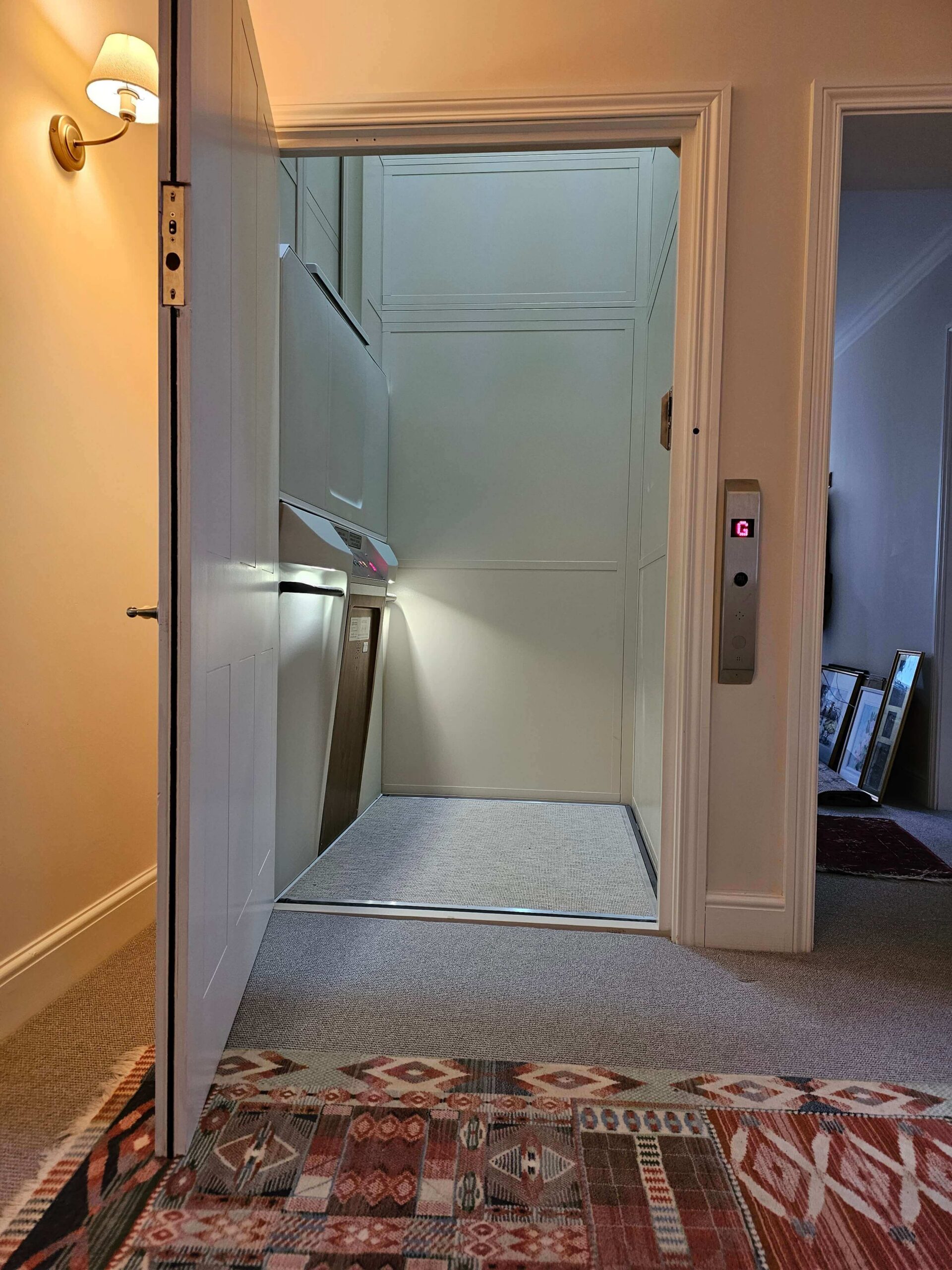 British Style vertical platform lift with doors open, wall-mounted call panel visible