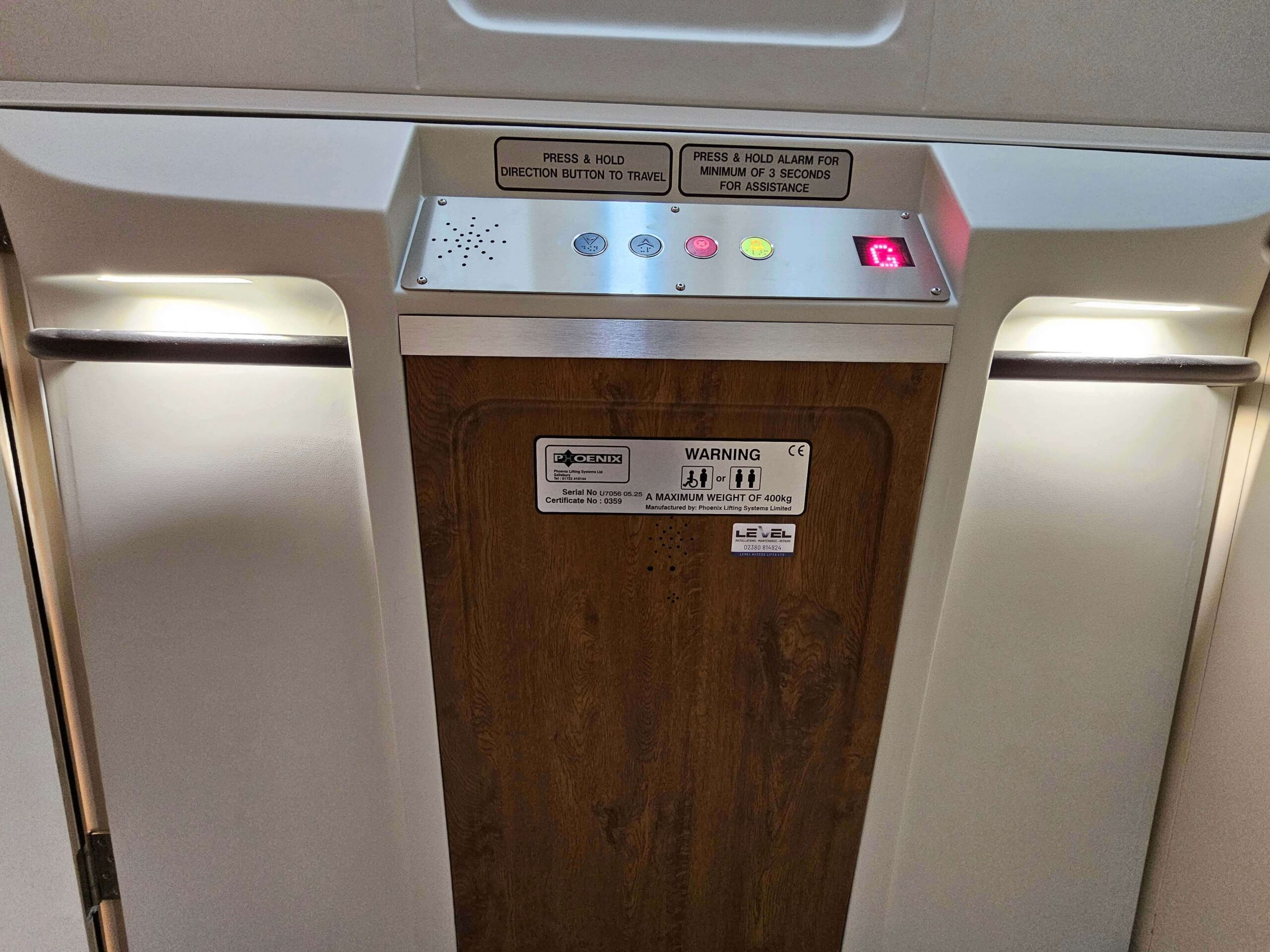 Close-up of the British Style vertical platform lift control panel and bespoke timber inner door, with stainless steel handrails either side.