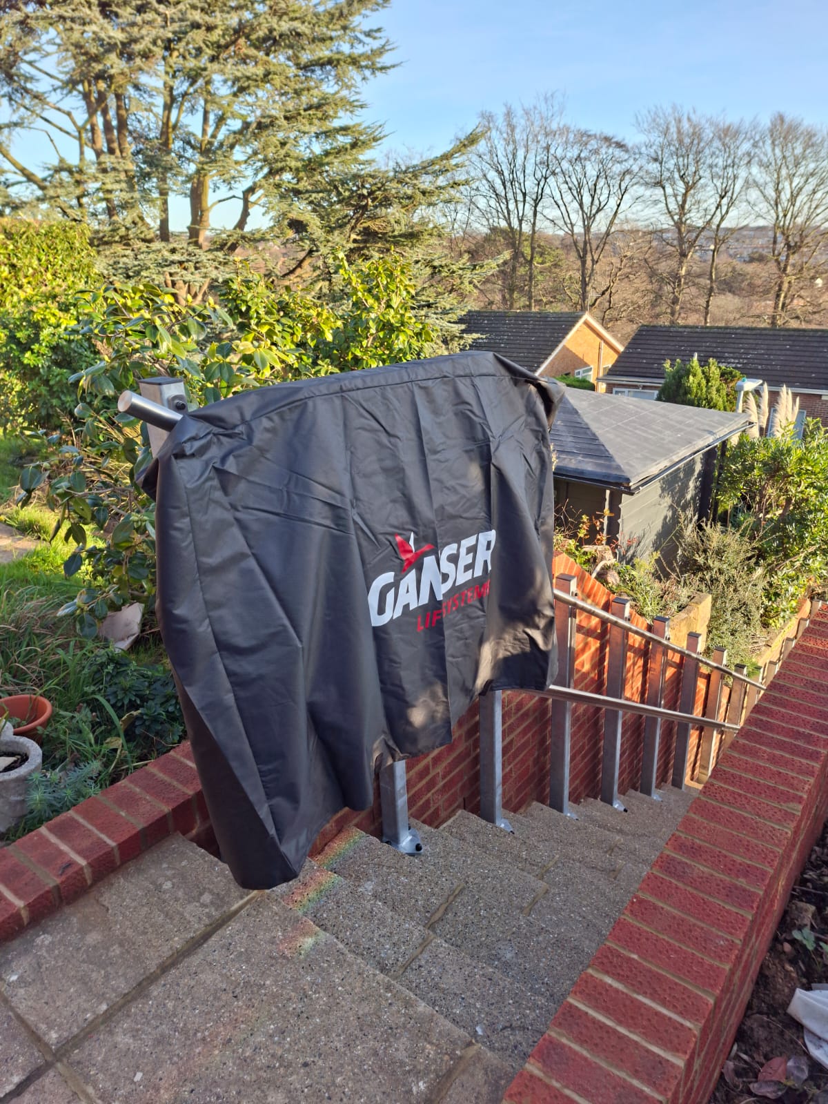Ganser GLTE inclined platform lift fitted with a black weatherproof protective cover on a steep flight of outdoor residential steps