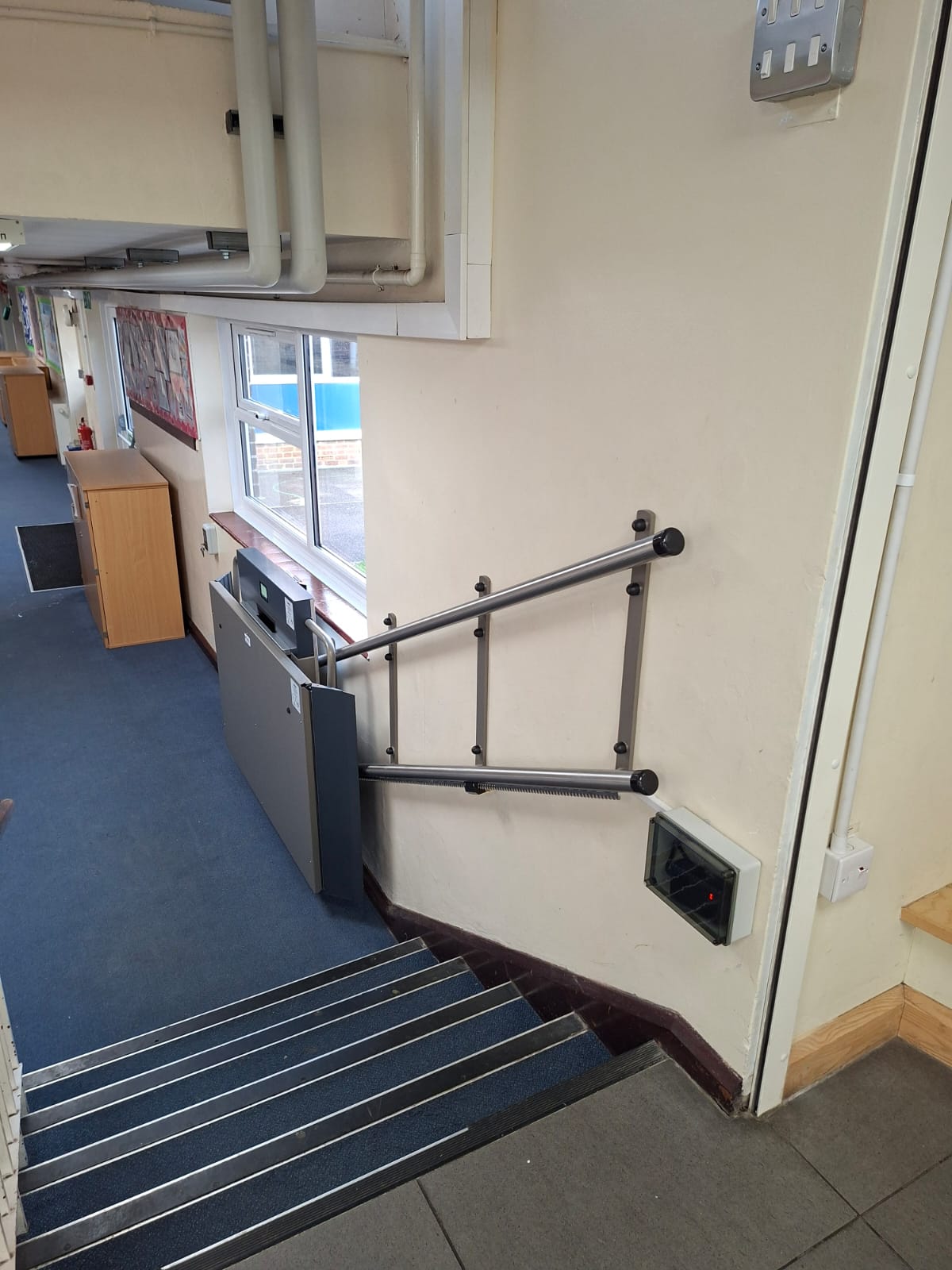 Upper landing view of GTLE platform stair lift installation showing staircase and call controls at Laurel Lane Primary School