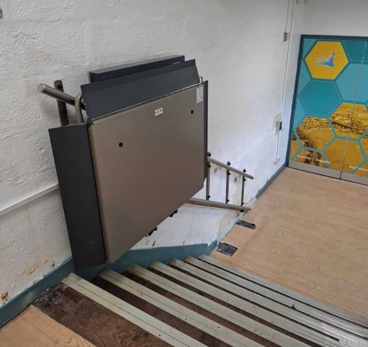 Wall-mounted GTLE Platform Stair Lift folded up, Saltash Community School.