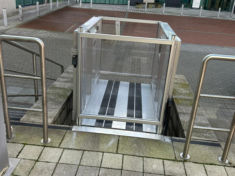 Tech Lift M4 external step lift at lower level at Colton Square, Leicester, with call button panel on the retaining wall and office entrance visible behind