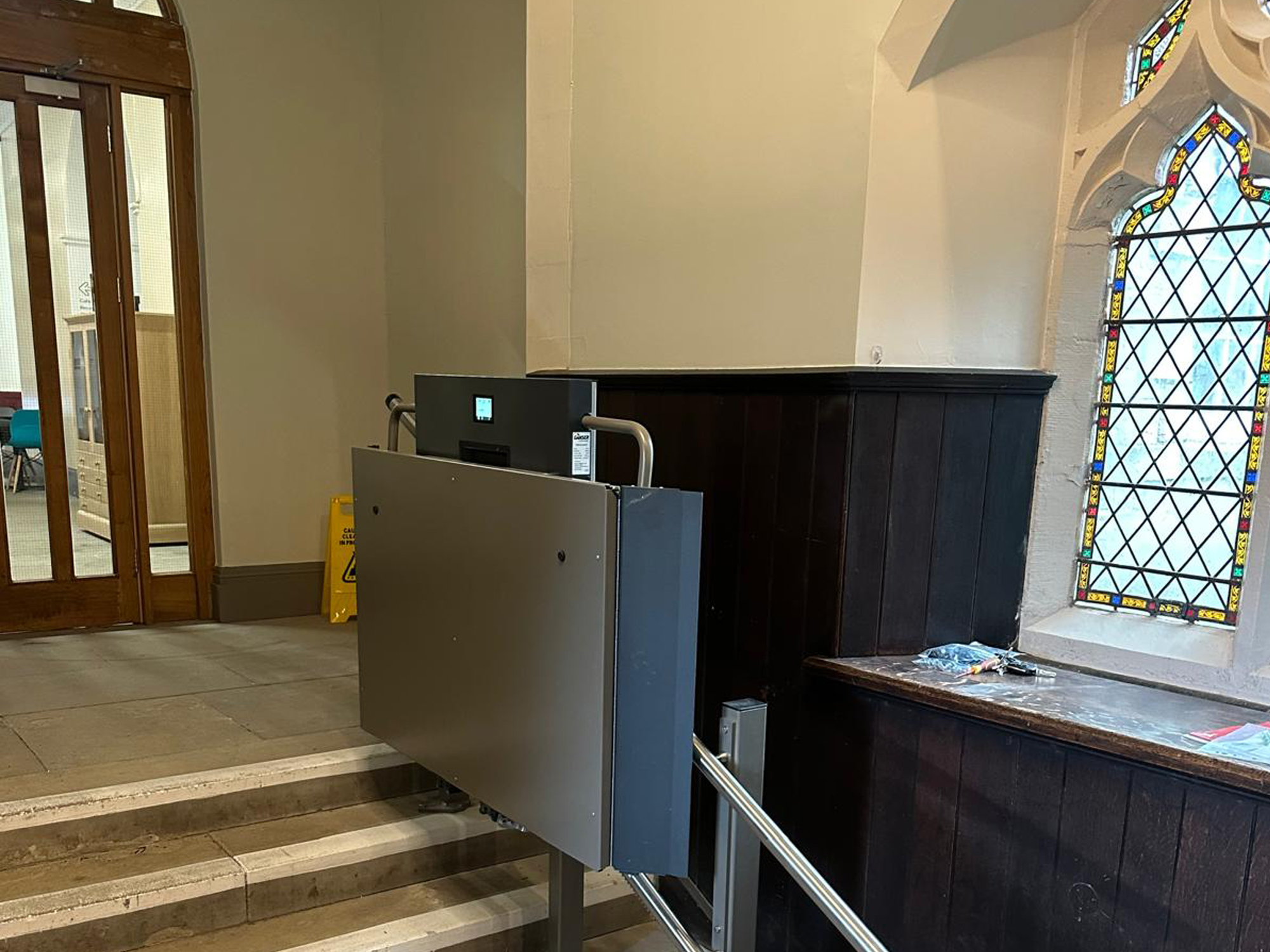 GTLE platform stair lift in parked position beside chapel pew panelling, Ushaw Historic House