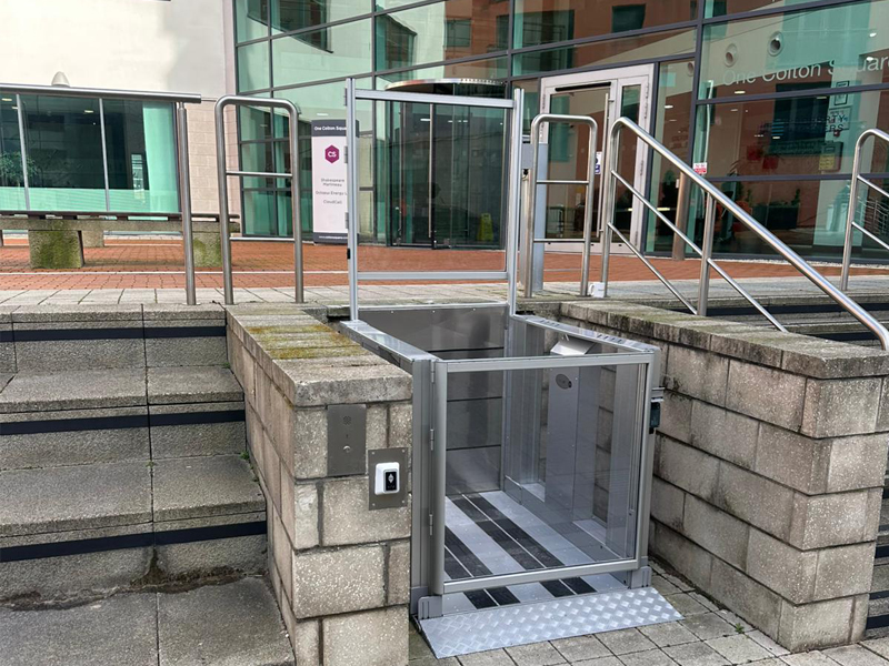 Tech Lift M4 external step lift at Colton Square, Leicester, showing the full structure with glazed panels against the backdrop of the surrounding commercial development
