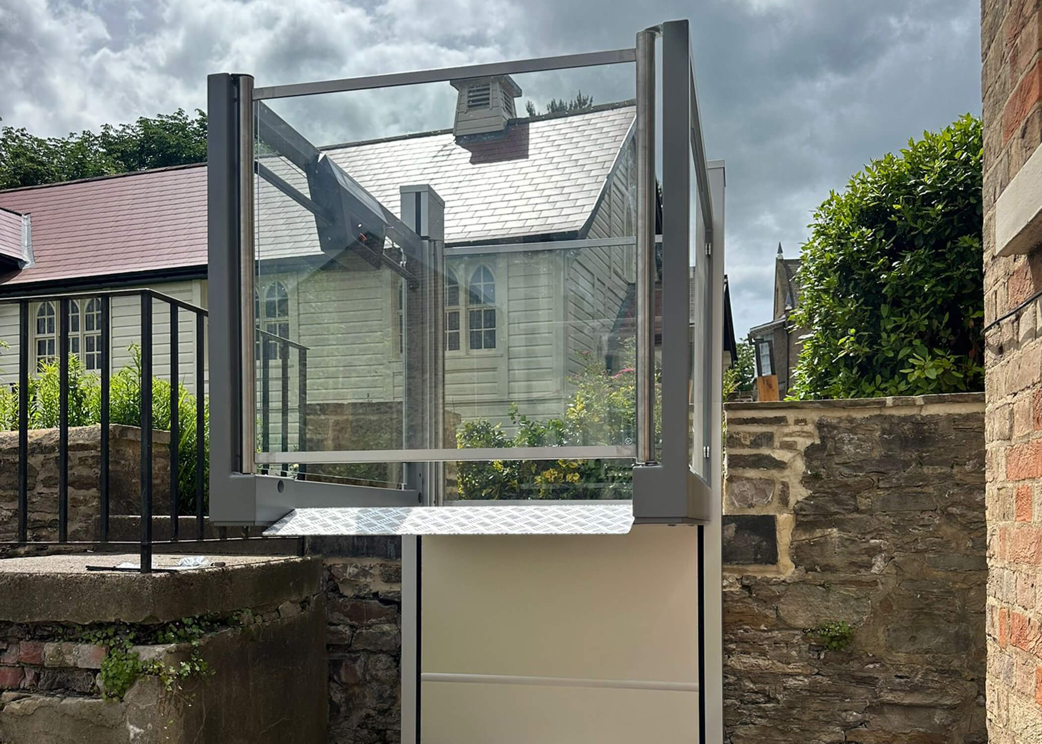 UnaPorte platform lift raised to full height at St Chad's College, with frameless glass sides against a historic chapel backdrop