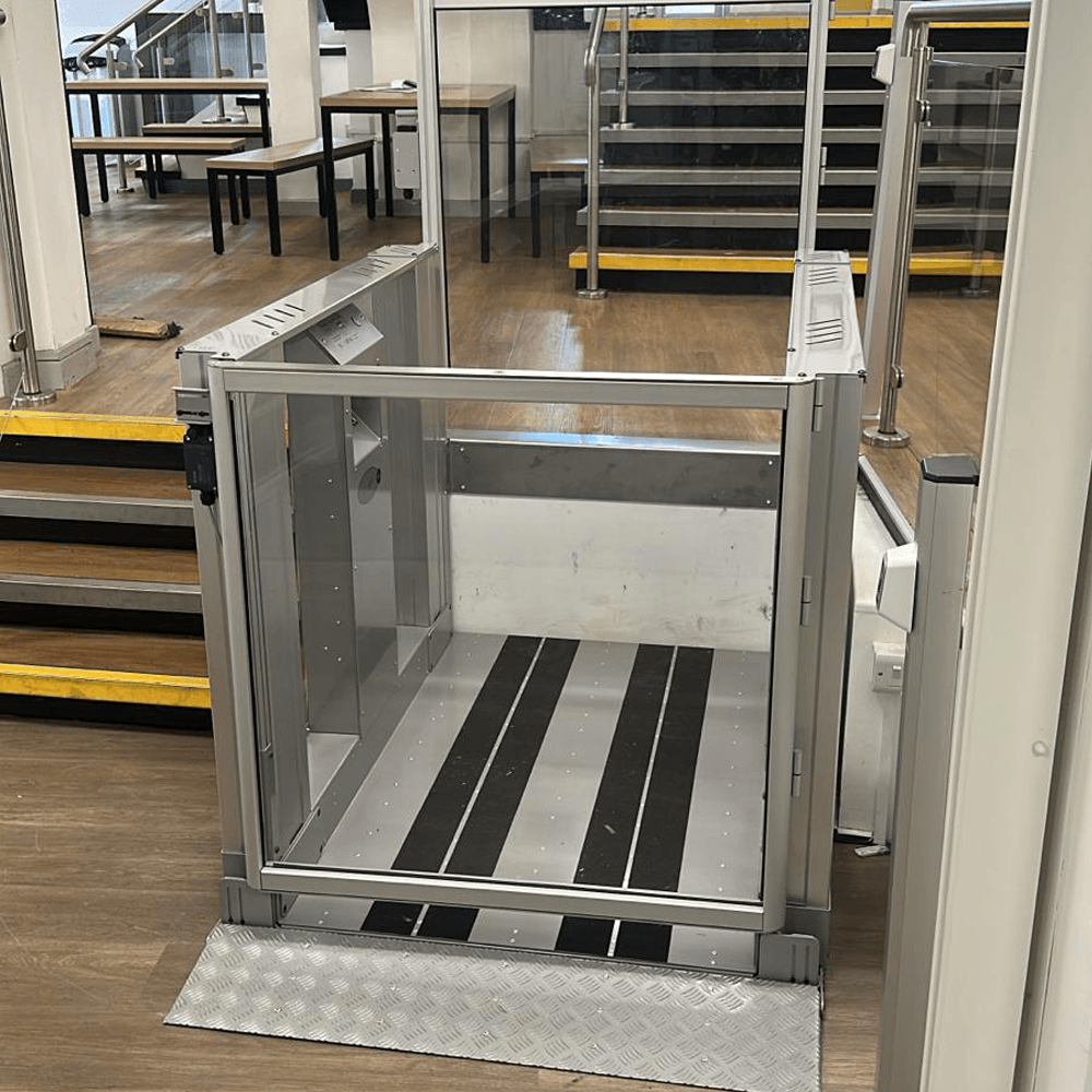 Silver aluminium step lift at its lower level with a chequer plate threshold plate, at Stamford College.